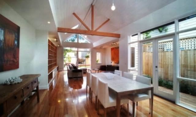 A finished Household renovation: open-plan living and dining room with a raked timber-truss ceiling, timber floors and glazed doors to the garden